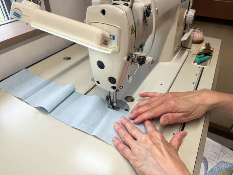 作業手順①スカート生地の上から約5mmの位置を、ミシンの縫い目を最大にして直線縫いしている様子