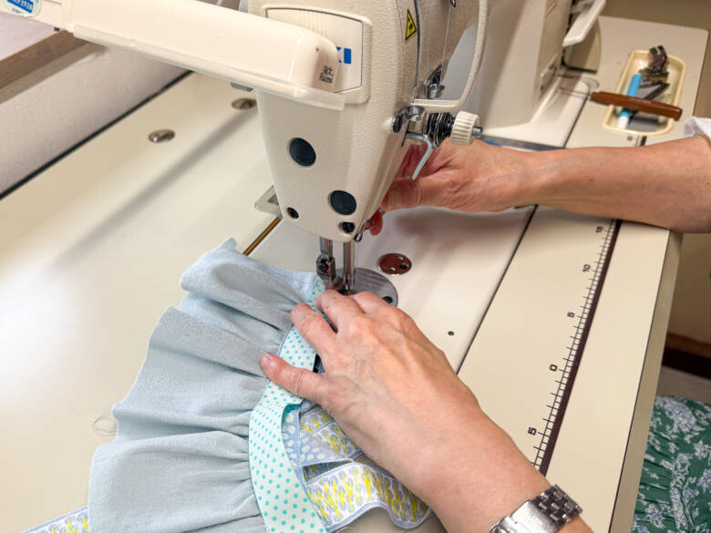 ⑧ 胸のチロルリボンの上に、中表でリバーシブルリボンを重ね、両端を縫い代1cmで縫い合わせたあと、表に返す様子