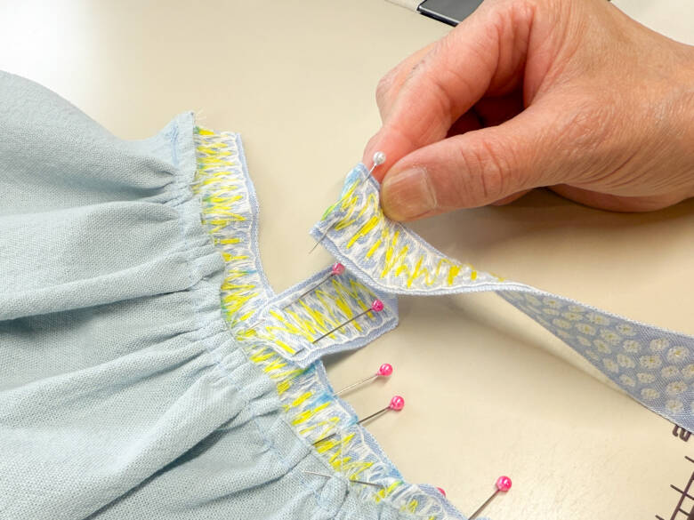 作業手順⑥ 肩ひも用のチロルリボンを、印の位置に1cm内側に差し込むように置き、待ち針でとめた様子