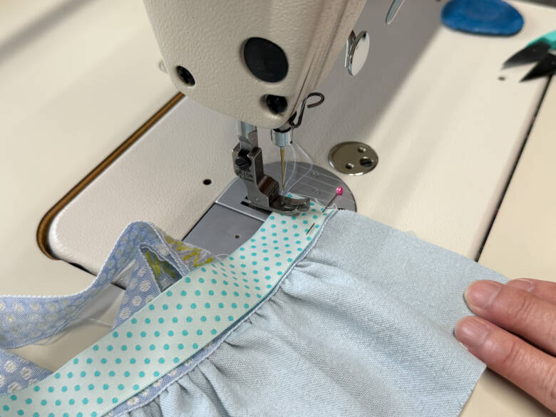 ⑧ 胸のチロルリボンの上に、中表でリバーシブルリボンを重ね、両端を縫い代1cmで縫い合わせたあと、表に返す様子