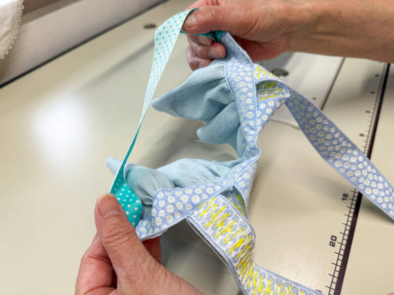 ⑧ 胸のチロルリボンの上に、中表でリバーシブルリボンを重ね、両端を縫い代1cmで縫い合わせたあと、表に返す様子