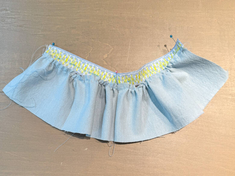 作業手順③ ②で引いたラインの上に、①で作ったスカートを乗せ、糸を引っぱってギャザーを寄せた様子。ギャザーが均等になるように調整しながら待ち針でとめる