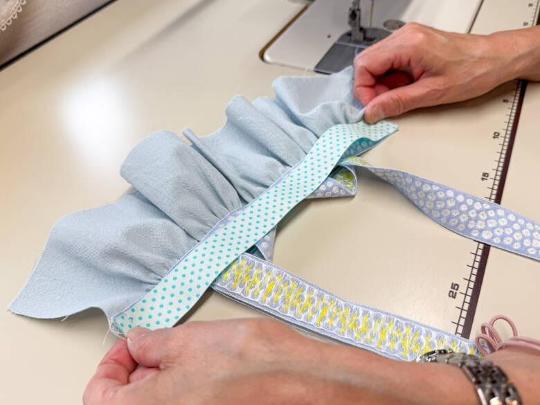 ⑧ 胸のチロルリボンの上に、中表でリバーシブルリボンを重ね、両端を縫い代1cmで縫い合わせたあと、表に返す様子